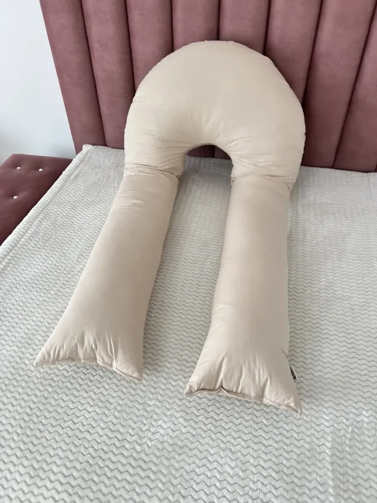 U-shaped pregnancy pillow in beige, laid out on a bed
