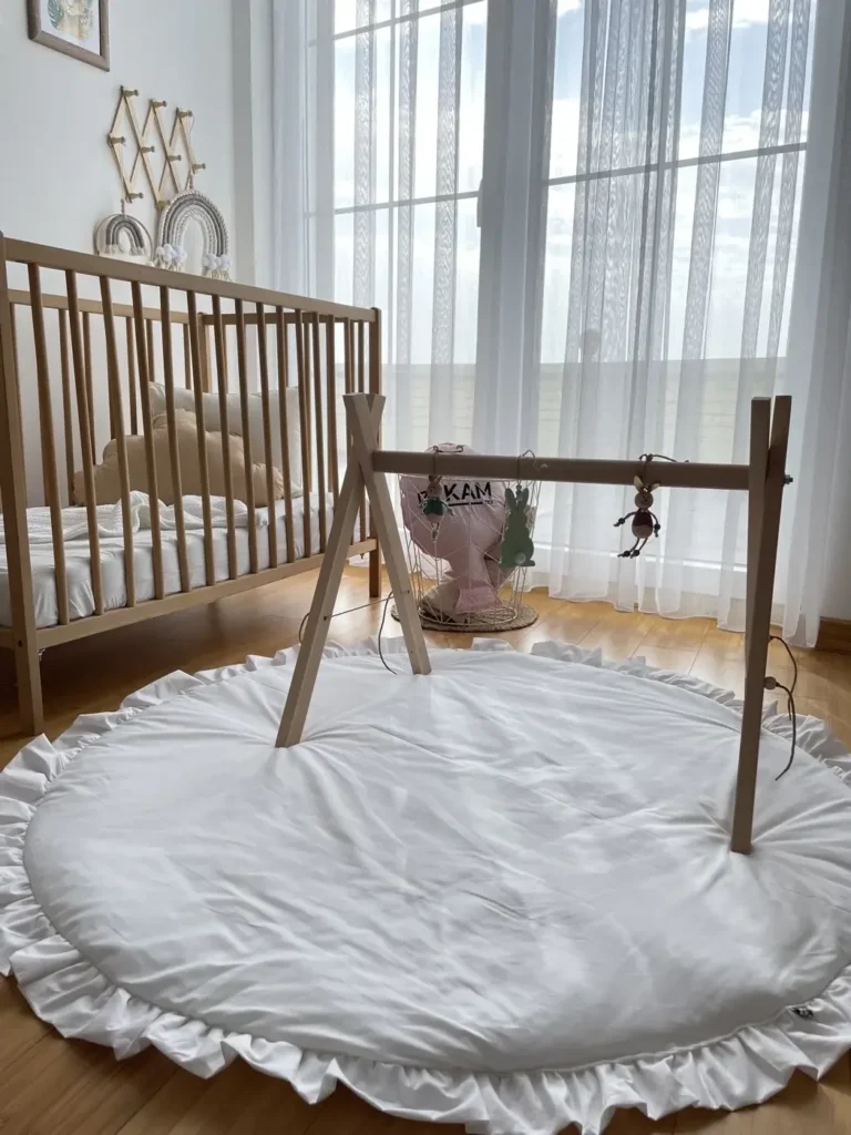 Wooden baby play gym with hanging toys over a white ruffled play mat on the floor